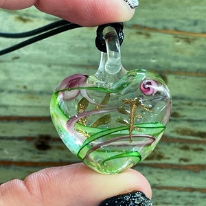 May include: A green glass heart pendant with gold and pink swirls inside. The pendant is on a black cord.
