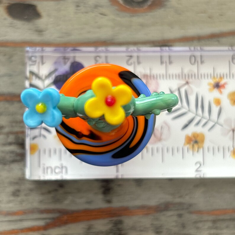 May include: A glass figurine of a cactus with two yellow flowers and one blue flower. The cactus is green and the base is orange, black, and blue.