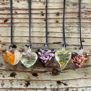 May include: Six glass heart pendants on black cords, each with a different colorful design. The hearts feature swirls, floral patterns, and abstract designs.