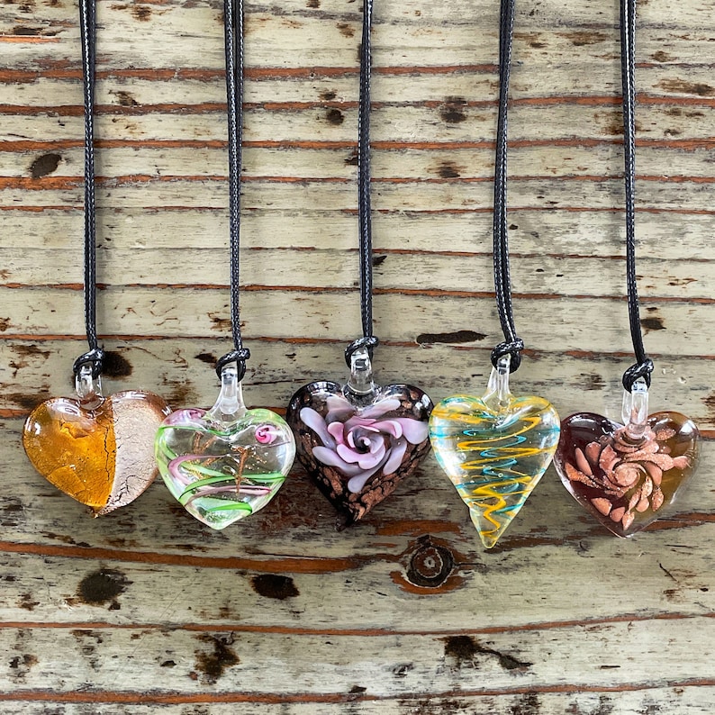 May include: Six glass heart pendants on black cords, each with a different colorful design. The hearts feature swirls, floral patterns, and abstract designs.