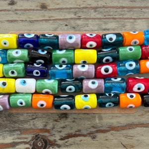 May include: A collection of colorful glass beads with an evil eye design. The beads are arranged in a row and feature various colors, including blue, green, red, yellow, and orange.