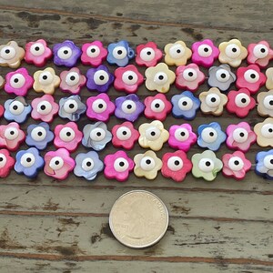 May include: A collection of colorful flower-shaped beads with an evil eye design. The beads are made of mother of pearl and have a white eye with a black pupil. The beads are arranged in rows on a wooden surface.