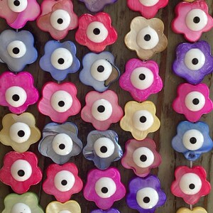 May include: A string of colorful flower-shaped beads with an evil eye charm in the center of each bead. The beads are made of mother of pearl and have a glossy finish.