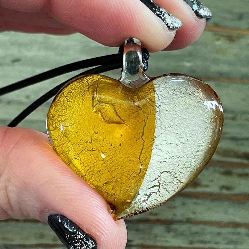 May include: A heart-shaped glass pendant with a gold and white crackle finish. The pendant is attached to a black cord.