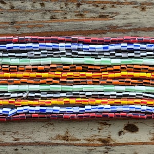 Puede incluir: Primer plano de un collar de cuentas de colores con filas alternas de cuentas rojas, naranjas, amarillas, verdes, azules y negras. Las cuentas están dispuestas en un patrón de tablero de ajedrez.