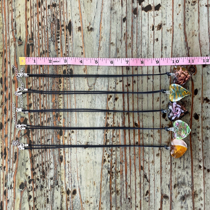 May include: Five black necklaces with silver clasps and colorful glass heart pendants. The pendants feature floral designs and are approximately 1 inch in size.