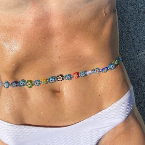 May include: A colorful waist bead strand featuring small, flower-shaped beads in various colors. The beads are strung together, creating a decorative accessory. The image shows the waist beads worn over a white bikini bottom.