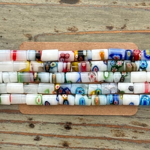 May include: A close-up of a collection of colorful glass beads. The beads are white with a variety of colorful patterns and designs. The beads are arranged in a row on a wooden surface.