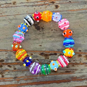 May include: A colorful beaded bracelet featuring a variety of glass beads in vibrant colors. The beads are round with striped, dotted, and textured designs. The bracelet is a playful accessory.