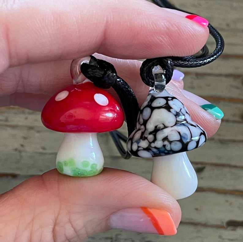 May include: A black cord necklace with two glass mushroom pendants. One mushroom is red with white dots and the other is black and white with a marbled pattern.