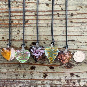 May include: Six glass heart pendants on black cords. The hearts are all different colors and designs, including gold, green, pink, and blue.