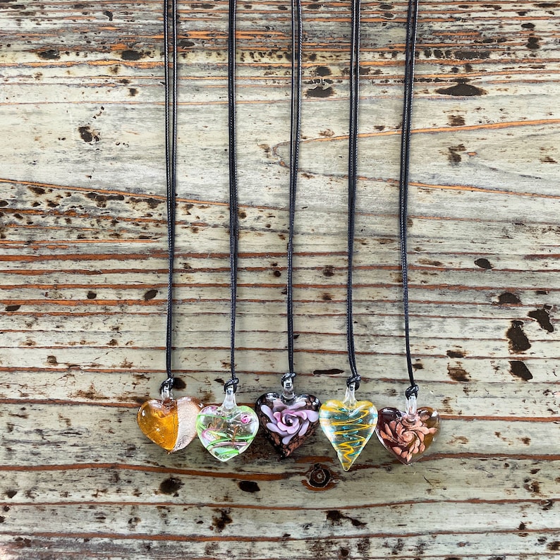 May include: Five glass heart pendants on black cords. The hearts are all different colors and designs, including yellow, green, pink, and brown.