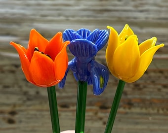 Könnte beinhalten: Drei Glasstiel mit orangefarbenen, blauen und gelben Glasblumen. Die Blumen sind aus Glas und haben ein realistisches Aussehen.