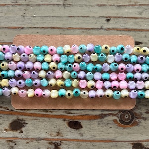 May include: A strand of colorful glass beads with an eye design. The beads are translucent and have a variety of colors, including pink, yellow, blue, and purple.