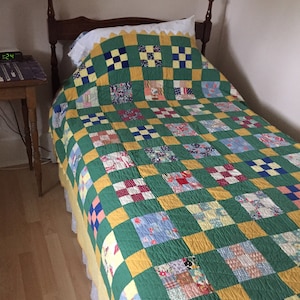 May include: A green and yellow patchwork quilt with a white ruffle on a wooden bed frame.