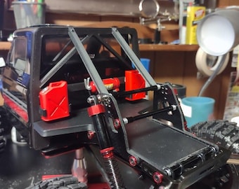 May include: Black and red remote control truck with large, knobby tires. The truck features a roll cage, red accents, and two red fuel canisters. The suspension system is visible, with red springs and black shocks.