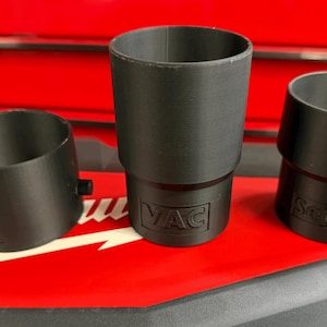 Puede incluir: Tres accesorios negros de plástico para aspiradora. Uno es cilíndrico, otro está en ángulo y el tercero es un cilindro más corto. Los accesorios están sobre una superficie roja con la palabra "VAC" visible.