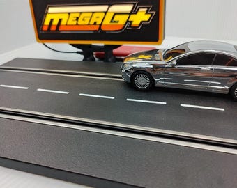 May include: A silver toy car on a black track with white lane markings. The track has a sign that reads "MEGA G+" in yellow and orange. The car is a coupe style.