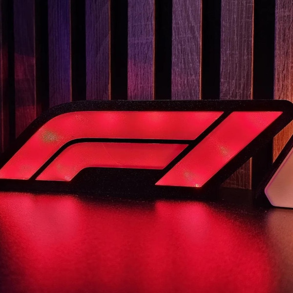 Puede incluir: Un logotipo de Fórmula 1 rojo brillante con un borde negro. El letrero emite una luz roja, que se refleja en la superficie. El fondo presenta listones de madera verticales.