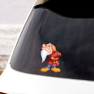 May include: A white car with a cartoon sticker of a dwarf character on the back window. The dwarf is wearing a red and blue outfit and has a white beard.
