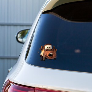 Peut inclure: Une voiture blanche avec un autocollant de personnage de d&eacute;panneuse orange rouill&eacute; sur la vitre arri&egrave;re. Le personnage a une expression surprise, la bouche ouverte et les yeux &eacute;carquill&eacute;s.