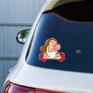 May include: A vinyl decal sticker featuring a cartoon character with a brown hat, white beard, and a large pink nose, wearing a red shirt with gold accents. The character has a grumpy facial expression with furrowed brows and crossed arms.