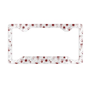 May include: A rectangular license plate frame featuring a white background with a repeating pattern of dark red blood splatters, drips, and handprints. The frame has four mounting holes, one in each corner, and a wide border design.