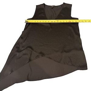 Peut inclure: Un haut noir sans manches avec un col en V. Le haut a un ourlet asym&eacute;trique, avec un panneau arri&egrave;re plus long. Une mesure avec un m&egrave;tre ruban jaune indique une longueur d'environ 58 cm.