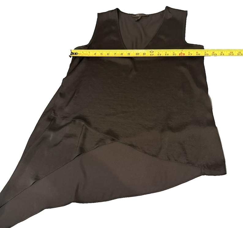 Peut inclure: Un haut noir sans manches avec un col en V. Le haut a un ourlet asym&eacute;trique, avec un panneau arri&egrave;re plus long. Une mesure avec un m&egrave;tre ruban jaune indique une longueur d'environ 58 cm.