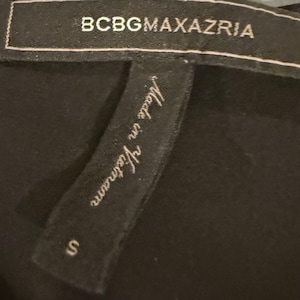 Peut inclure: Gros plan sur une &eacute;tiquette de v&ecirc;tement noire avec le nom de la marque BCBGMAXAZRIA en lettres blanches. L'&eacute;tiquette indique &eacute;galement "Made in Vietnam" et la taille "S".