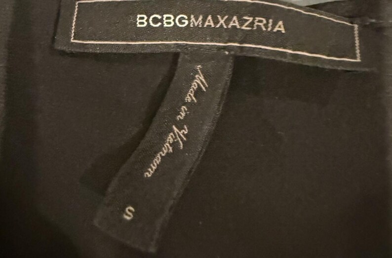 Peut inclure: Gros plan sur une &eacute;tiquette de v&ecirc;tement noire avec le nom de la marque BCBGMAXAZRIA en lettres blanches. L'&eacute;tiquette indique &eacute;galement "Made in Vietnam" et la taille "S".