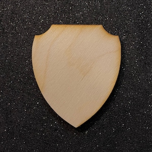 May include: A plain wooden shield with a slightly rounded top and bottom. The shield is light brown and has a smooth surface.