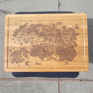 May include: A rectangular bamboo cutting board with a detailed map of a fantasy world engraved on its surface. The map features intricate landmasses, islands, and text. The board has a natural wood grain and a raised edge.
