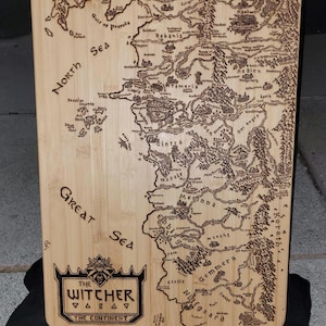 Puede incluir: Tabla de cortar rectangular de bambú con un mapa detallado de The Continent de la serie The Witcher, grabado en marrón. La tabla presenta texto que incluye "North Great Sea" y "The Witcher The Continent".