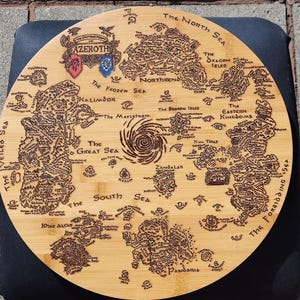 May include: A round, light brown wooden serving tray with a detailed map of Azeroth, featuring various regions and seas. The map is intricately etched into the wood, with text labels and decorative elements. The tray includes the text "The Shattering of Azeroth".