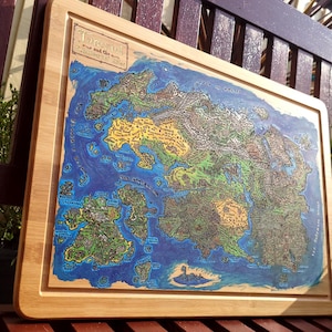 May include: A rectangular bamboo chopping board featuring a detailed, colourful fantasy map printed on its surface. The map displays various islands, mountain ranges, and bodies of water, with the text "Tamriel" visible in the upper left corner.