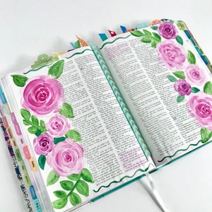 May include: A close-up of an open Bible with watercolor painted pink roses and green leaves on the left page. The right page has text from the book of Psalms, verses 36-38. The pages are decorated with colorful washi tape.