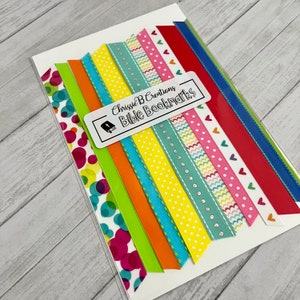 May include: A set of 10 colorful ribbon bookmarks with various patterns, including polka dots, hearts, and waves. The ribbons are packaged on a white card with the text "Chrissie B Creations Bible Bookmarks".