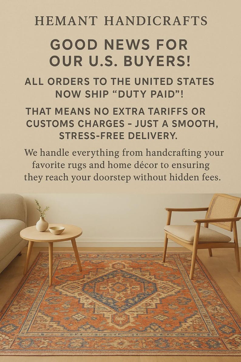 May include: An orange and blue patterned rug is the focal point of a living room scene. The room includes a wooden side table with a vase and bowl, a beige sofa, and a wooden chair. Text in the image reads "HEMANT HANDICRAFTS" and "GOOD NEWS FOR OUR U.S. BUYERS!"