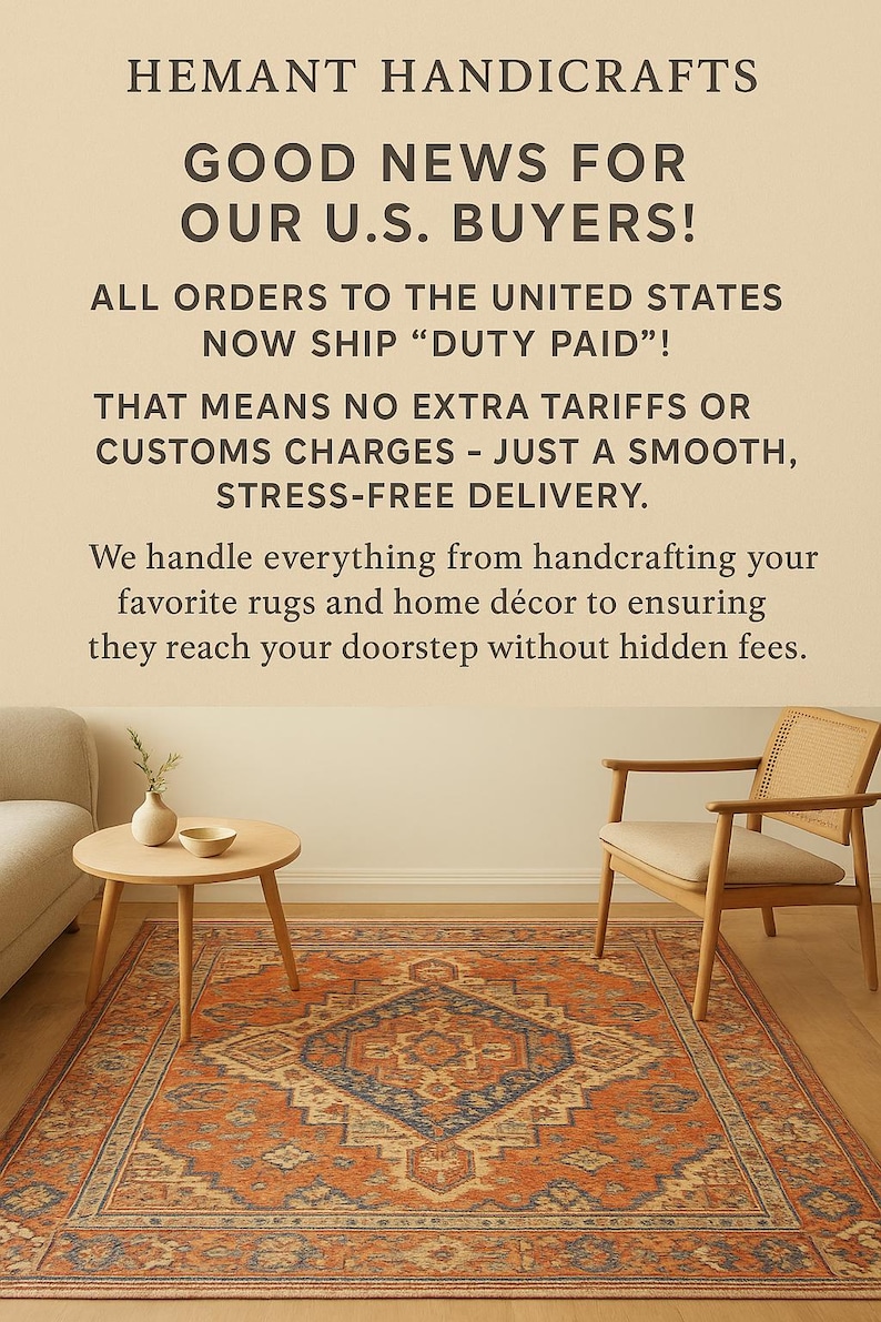 May include: A rectangular area rug with a central blue diamond pattern on an orange background, featuring intricate borders. The rug is placed in a room with a light wood chair, a small round table with a vase and bowl, and a portion of a sofa.