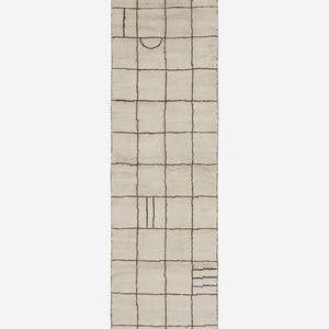May include: A rectangular runner rug in off-white featuring a dark brown grid pattern. The design includes irregular line segments, a semi-circle, and small parallel bars within the grid squares. The rug ends have short, light-colored fringe.