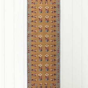 May include: A rectangular, mustard-colored runner rug with a repeating floral pattern in shades of red, blue, and white. The rug has a blue border and fringed edges. The design is symmetrical and traditional.