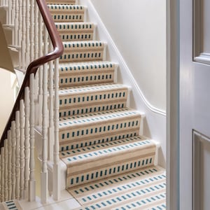 May include: A staircase with beige and blue striped carpet runners. The stairs have white risers and a dark brown wooden handrail. The balusters are white. The carpet pattern is repeated on the landing.