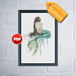 May include: Cross stitch pattern PDF for a mermaid with long brown hair and a green tail sitting on a white background with blue water droplets.