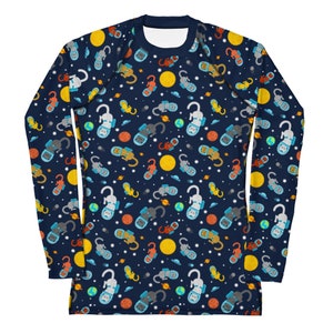 May include: A navy blue long-sleeved shirt with a repeating pattern of cats wearing astronaut helmets and floating in space. The pattern includes yellow suns, blue planets, and white stars.