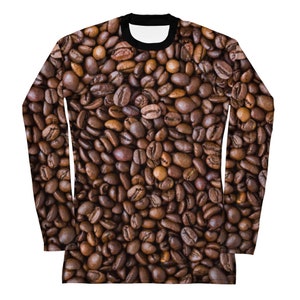 May include: Long-sleeved shirt featuring a detailed print of roasted coffee beans. The shirt has a black crew neck and a white inner collar. The coffee bean design covers the entire shirt, creating a textured, warm-toned appearance.
