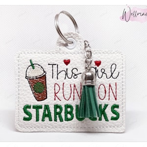 May include: White leather keychain with a green tassel and the text "This girl runs on Starbucks" in green and red embroidery. A cartoon image of a Starbucks coffee cup is also embroidered on the keychain.