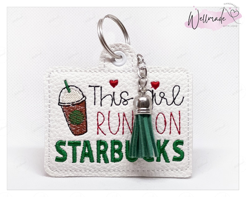 May include: White leather keychain with a green tassel and the text "This girl runs on Starbucks" in green and red embroidery. A cartoon image of a Starbucks coffee cup is also embroidered on the keychain.