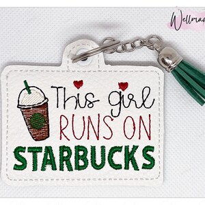 May include: White leather keychain with a green tassel and embroidered text that reads "This girl runs on Starbucks". The keychain features a red heart and a cartoon image of a Starbucks coffee cup.