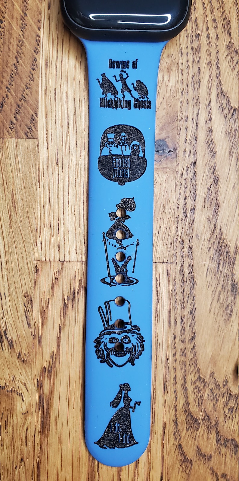 May include: A blue Apple Watch band with a black design featuring the text "Beware of Hitchhiking Ghosts" and images of characters from the Haunted Mansion attraction.